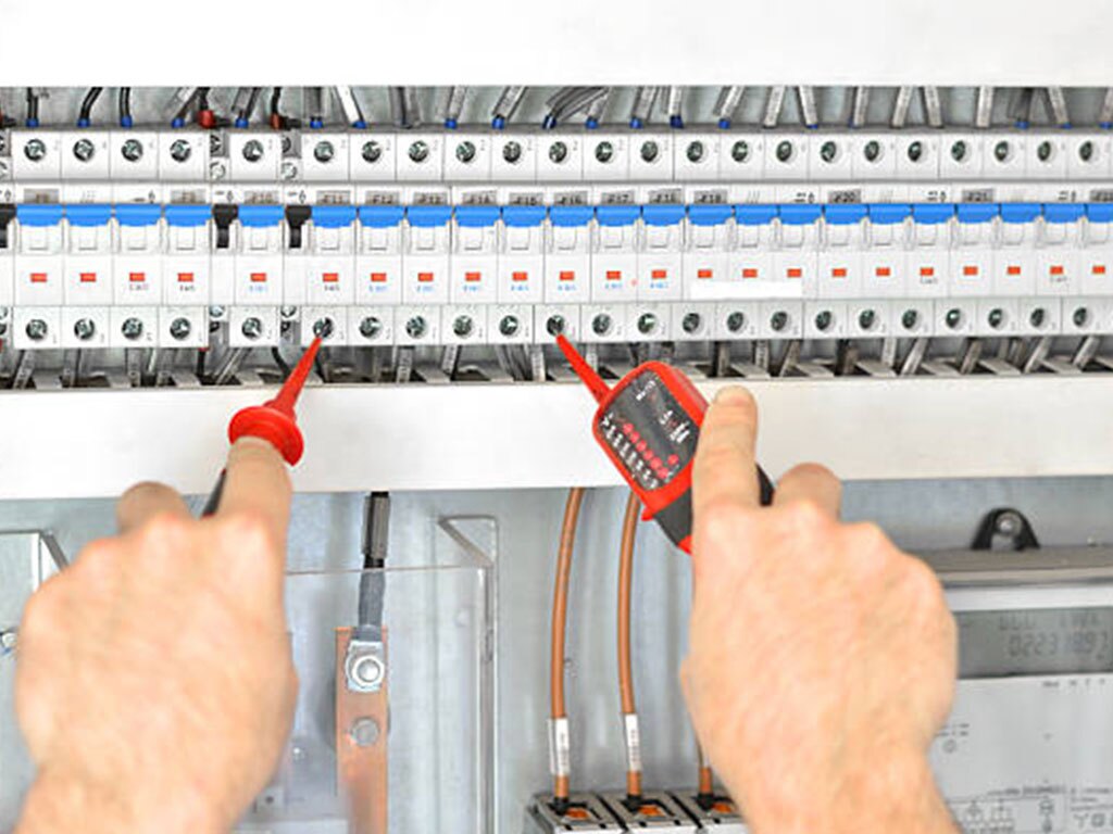 Hands of technician examining fusebox with multimeter probe